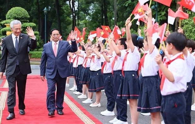 Prime Minister Pham Minh Chinh and his Singaporean counterpart Lee Hsien Loong (L) welcomed by children (Photo: VNA)